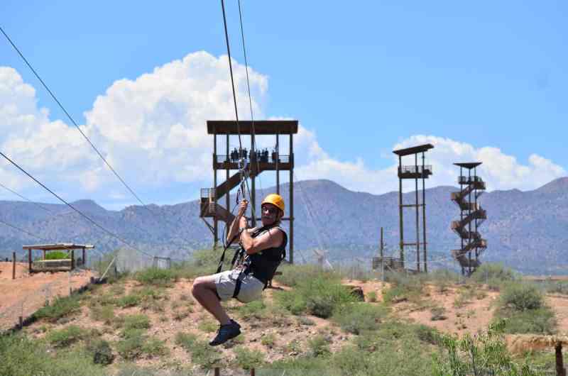 A man zip lining with the rest of the tour group on the tower behind him