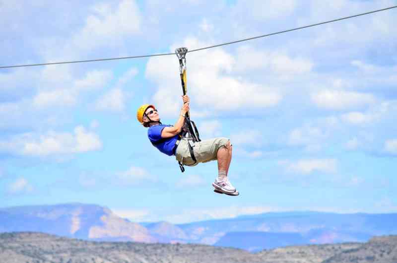 A zip liner leaning back and holding onto the harness